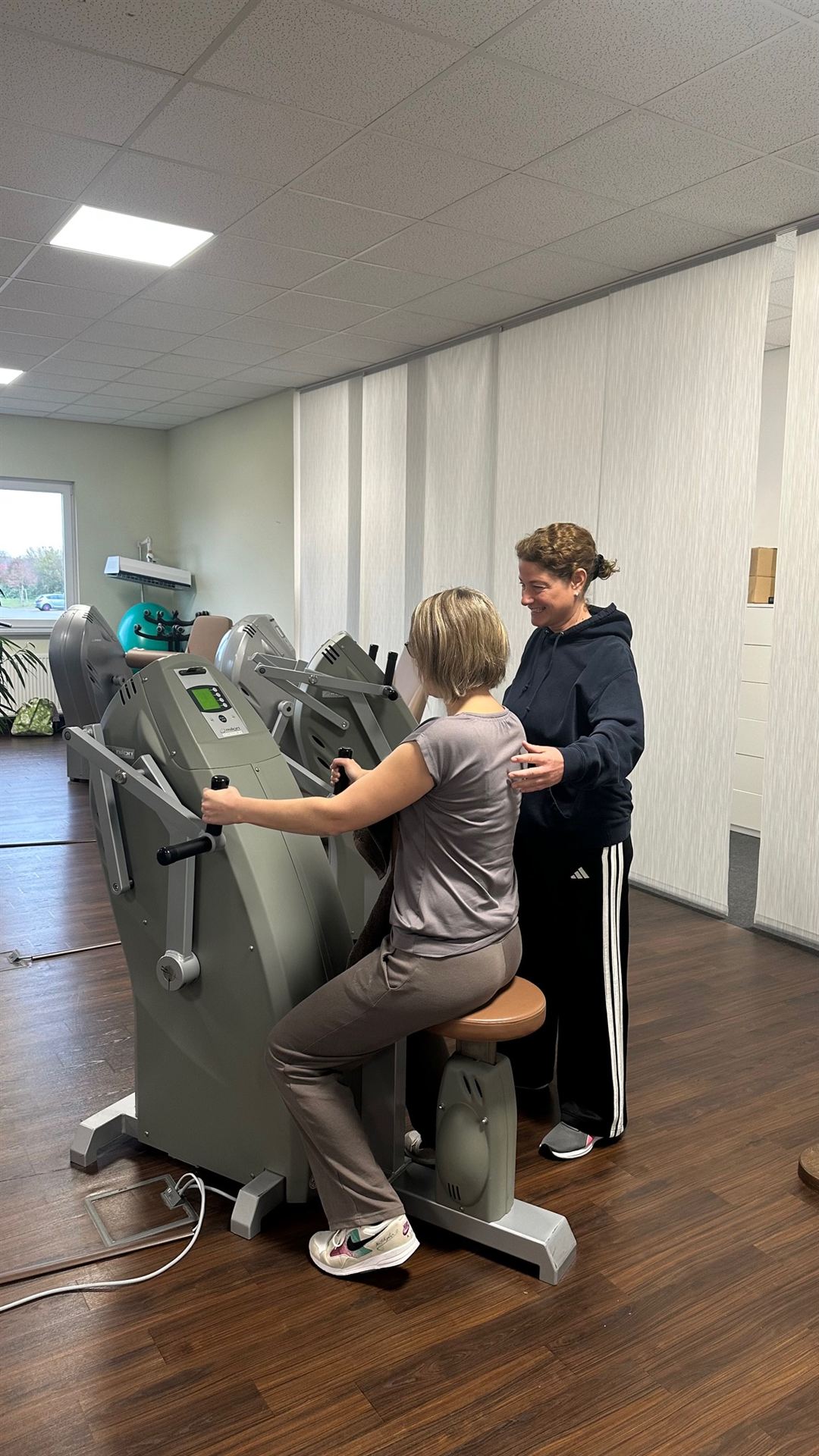 Physiotherapeutin begleitet lächelnd eine Patientin am Trainingsgerät
